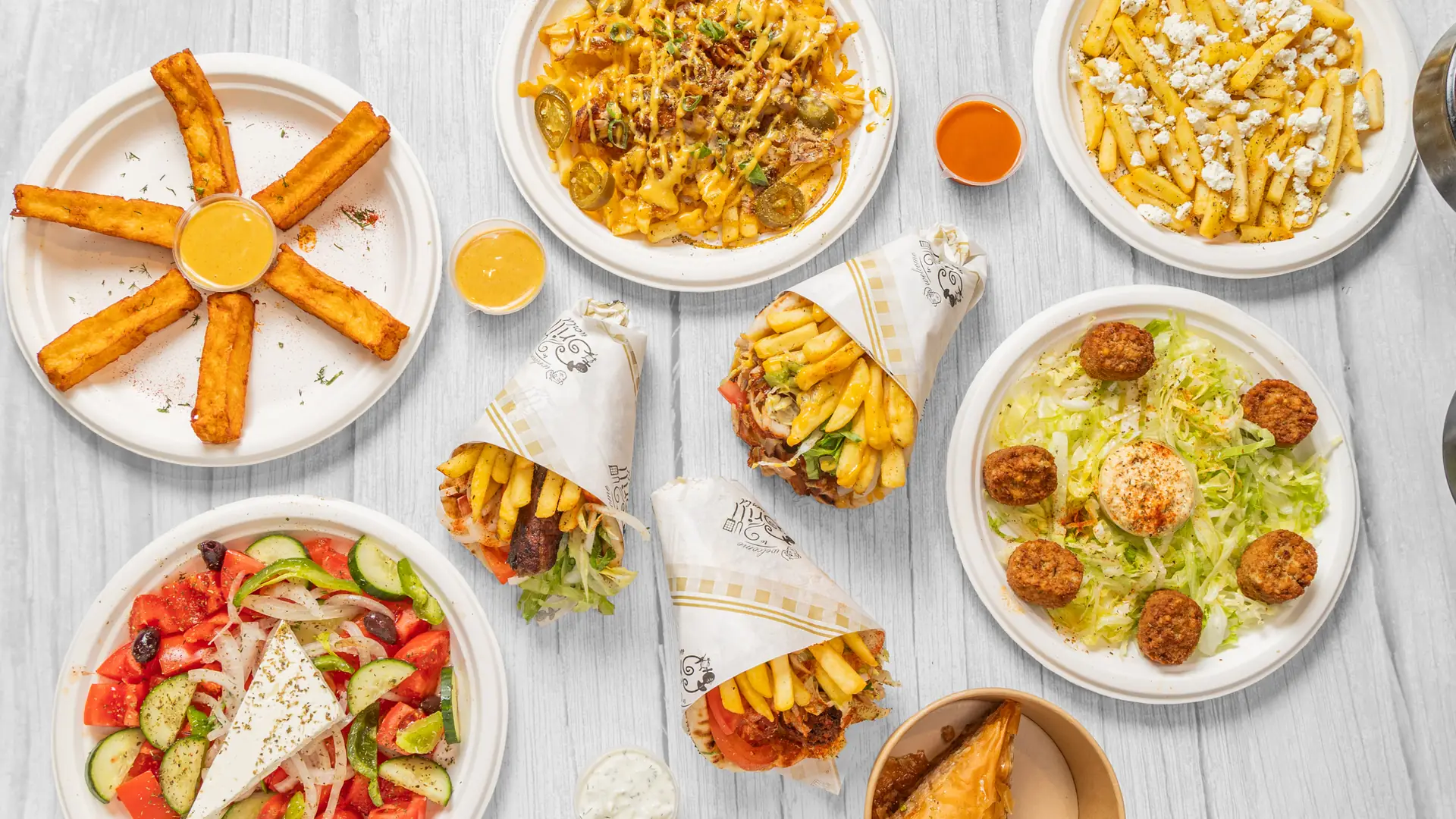 Overhead spread of Athens Original Gyros wraps, loaded fries, halloumi and Greek salad